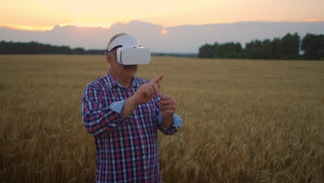 Ein-älterer-Erwachsener-Landwirt-Nutzt-Die-Virtuelle-Realität-Für-Die-Landwirtschaft,-Indem-Er-Mithilfe-Moderner-Technologie-Und-Grafiken-Ein-Ährchen-In-Den-Händen-Hält-Und-Mit-Dem-Finger-Auf-Das-Korn-Drückt.